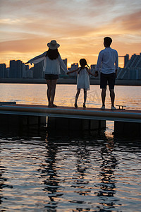 海边夕阳天空摄影照片_夕阳下一家三口在海边玩耍