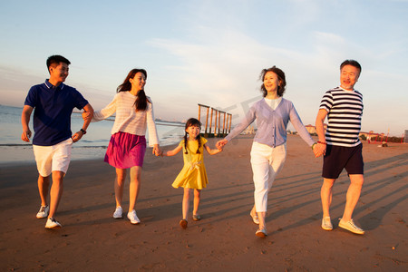 海边晚霞摄影照片_夕阳下在海边散步的幸福家庭