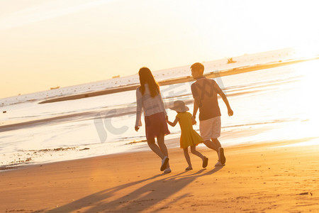 海边夕阳天空摄影照片_夕阳下一家三口在海边玩耍