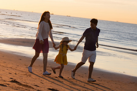夕阳下一家三口在海边玩耍