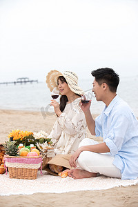 浪漫的青年夫妇坐在沙滩上喝红酒