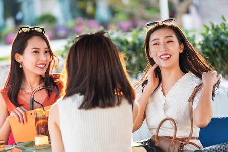 快乐的青年女人们坐在露天咖啡馆聊天