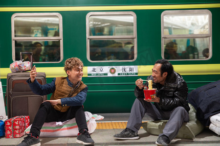回家的火车摄影照片_两名男子在火车月台上看手机