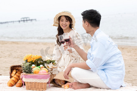 野炊摄影照片_浪漫的青年夫妇坐在沙滩上喝红酒