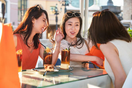快乐的青年女人们坐在露天咖啡馆分享购物成果