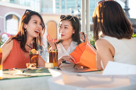 快乐的青年女人们坐在露天咖啡馆分享购物成果