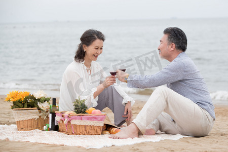 幸福的老年夫妇坐在海滩上野餐饮酒