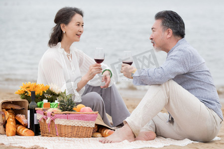 幸福的老年夫妇坐在海滩上野餐饮酒