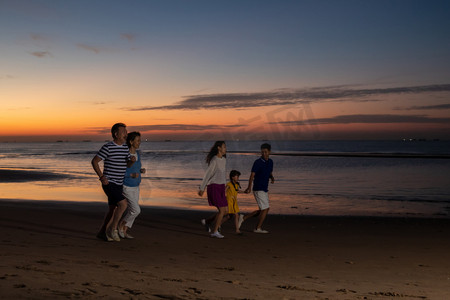 夕阳下在海边散步的幸福家庭