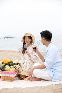 食品海边摄影照片_浪漫的青年夫妇坐在沙滩上喝红酒