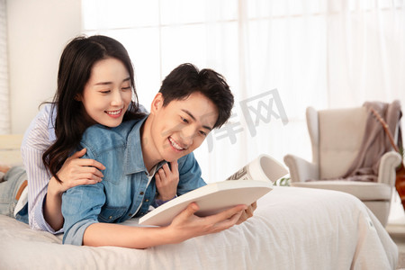 亲密的年轻情侣趴在床上看书