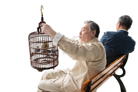 中式场景摄影照片_拿着鸟笼的老人和拿着手机的老人坐在长椅上