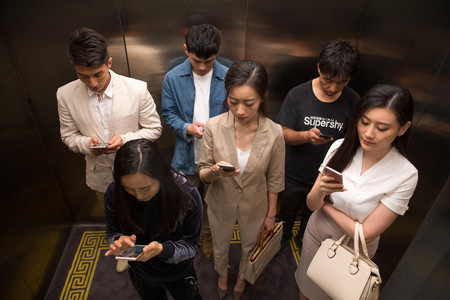 低头看手机的人摄影照片_商务青年男女乘电梯