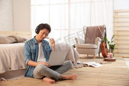 乐器图摄影照片_年轻的男青年坐在地板上使用笔记本电脑