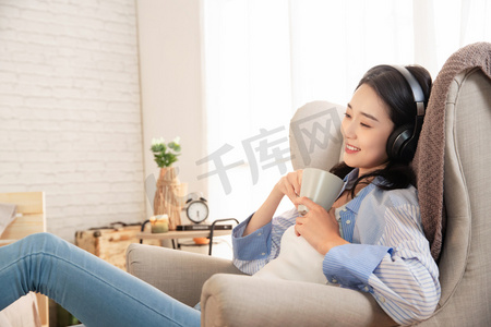 沙雕人物表情包摄影照片_快乐的女青年坐在沙发上听音乐
