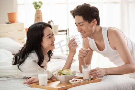 帅哥人物摄影照片_快乐的年轻情侣在床上吃早餐