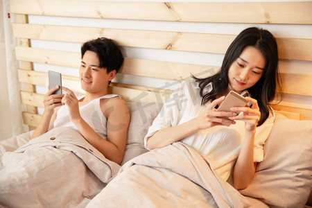 年轻情侣在床上使用手机