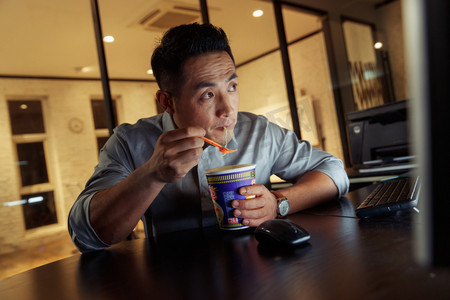 吃男摄影照片_在办公室加班吃方便面的青年男人
