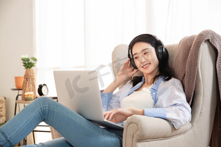 耳麦摄影照片_快乐的女青年坐在沙发上使用笔记本电脑