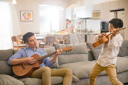 坐弹吉他摄影照片_父亲和男孩在弹吉他