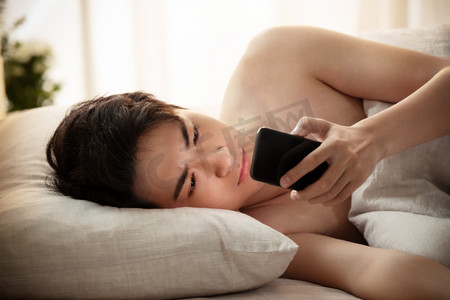 睡眠手机摄影照片_躺在床上玩手机的年轻男人