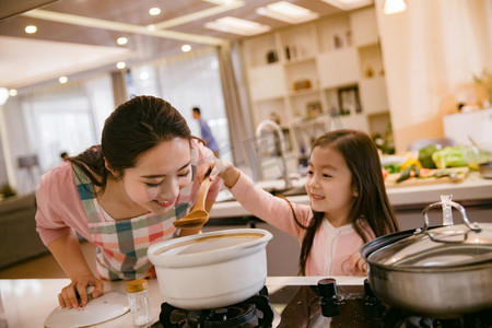 女人炒菜摄影照片_年轻妈妈和女儿在厨房
