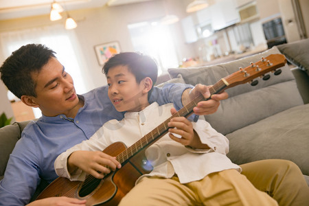 坐弹吉他摄影照片_父亲和男孩在弹吉他