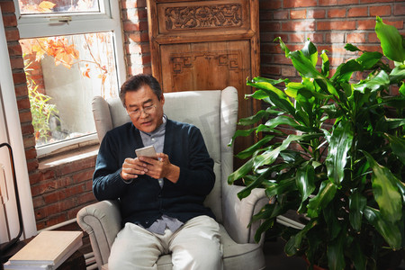 休闲的老年男人坐在家中玩手机