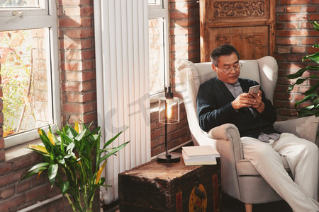 老人沙发摄影照片_休闲的老年男人坐在家中玩手机