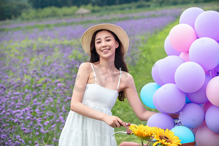 紫色气球摄影照片_青年女人在花海里骑自行车