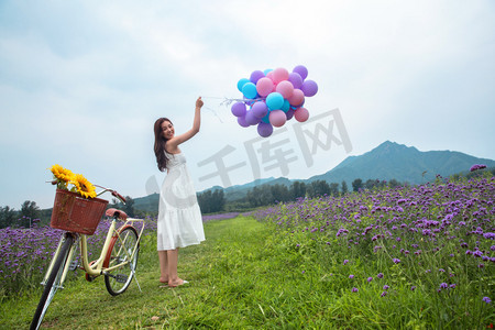 美女拿着花摄影照片_青年女人在花海里拿着气球