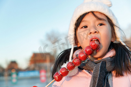 吃帽子摄影照片_快乐的小女孩吃糖葫芦