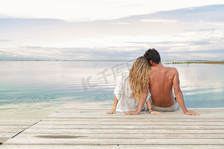 男人和女人的夫妻坐在码头在多云的蓝天下