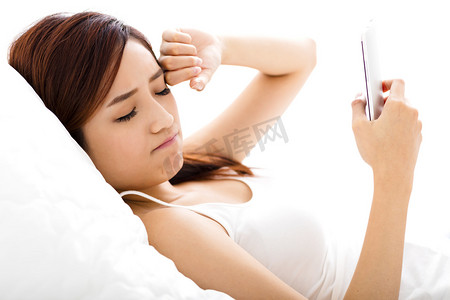 年轻的女人在床上用疲惫的眼神看智能手机