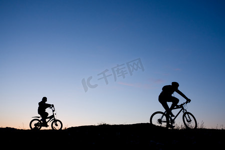 两个骑自行车的人反对日落-父亲和儿子的剪影
