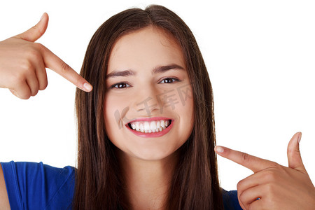 牙齿白化摄影照片_十几岁的女孩指着她完美的牙齿上