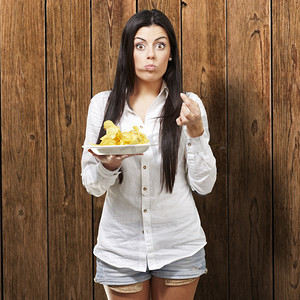 jovem摄影照片_年轻女人吃土豆薯条木制背景
