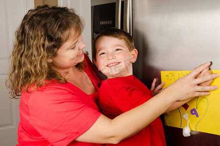 母亲和儿童家庭冰箱在家里上张贴男孩的艺术