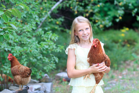农场鸡摄影照片_年轻的金发女孩在花园里与她鸡