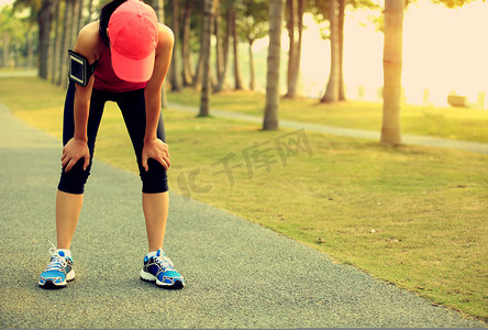 健身运动女摄影照片_累了的女跑步运动员休息后运行硬在热带公园径