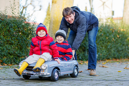 冬季户外男孩摄影照片_两个快乐同级男孩和父亲玩大旧玩具车, 