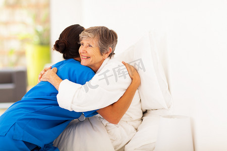 图标博士摄影照片_快乐老人的女人在床上拥抱照料者