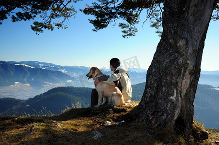 狗坐着摄影照片_男人和他的狗享受山景