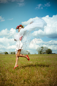 Girl in flower wreath with white shawl dancing on meadow