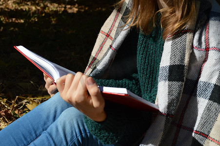 年轻、 漂亮的女孩裹在温暖的格子毛毯，喝热茶和读一本书在公园里