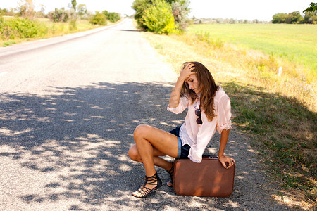 凄凉心情的摄影照片_绝望的女人坐在行李箱上乡村的道路