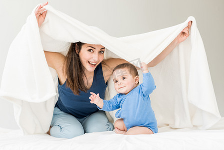 她笑的好开心摄影照片_母亲与她的儿子在毯子下玩 