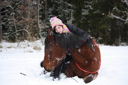 十几岁的女孩和匹棕色的马，躺在雪地里