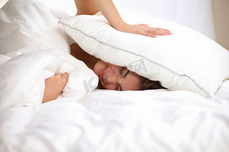 女性躺在床上和关闭她的耳朵用枕