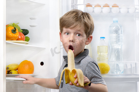 小可爱男孩吃香蕉附近打开冰箱